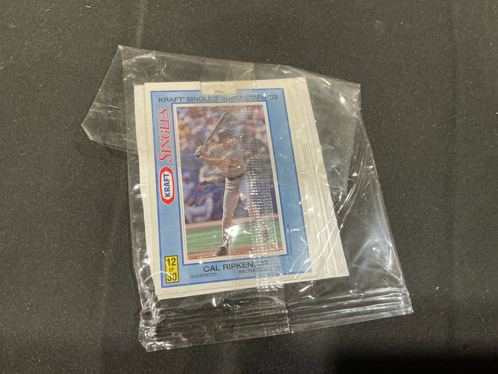 1993 Kraft Singles Superstars Cal Ripken Jr. Unopened Pack: Still contained in its original clear promotional wrapper, this 1993 Kraft Singles Superstars baseball card pack is fronted by Baltimore Orioles Hall of Famer Cal Ripken Jr., card #12 of 30. The