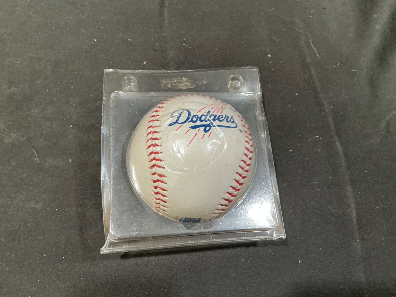 Los Angeles Dodgers Logo Baseball in Display Case: Los Angeles Dodgers memorabilia is represented by this white baseball bearing the classic blue Dodgers script logo with red accent graphics. Presented inside a clear hard plastic display case, the tea
