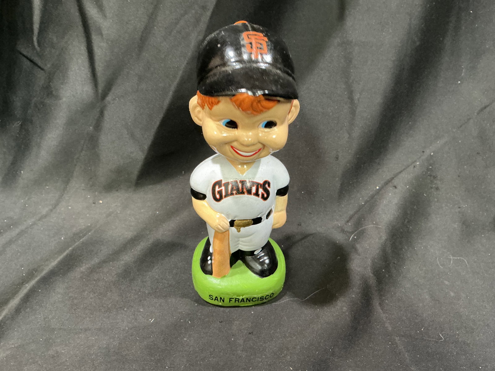 Vintage San Francisco Giants Bobblehead Bank: A vintage San Francisco Giants baseball bobblehead depicts a smiling red-haired player in a classic Giants uniform, black cap, and batting pose atop a bright green base marked "SAN FRANCISCO." The