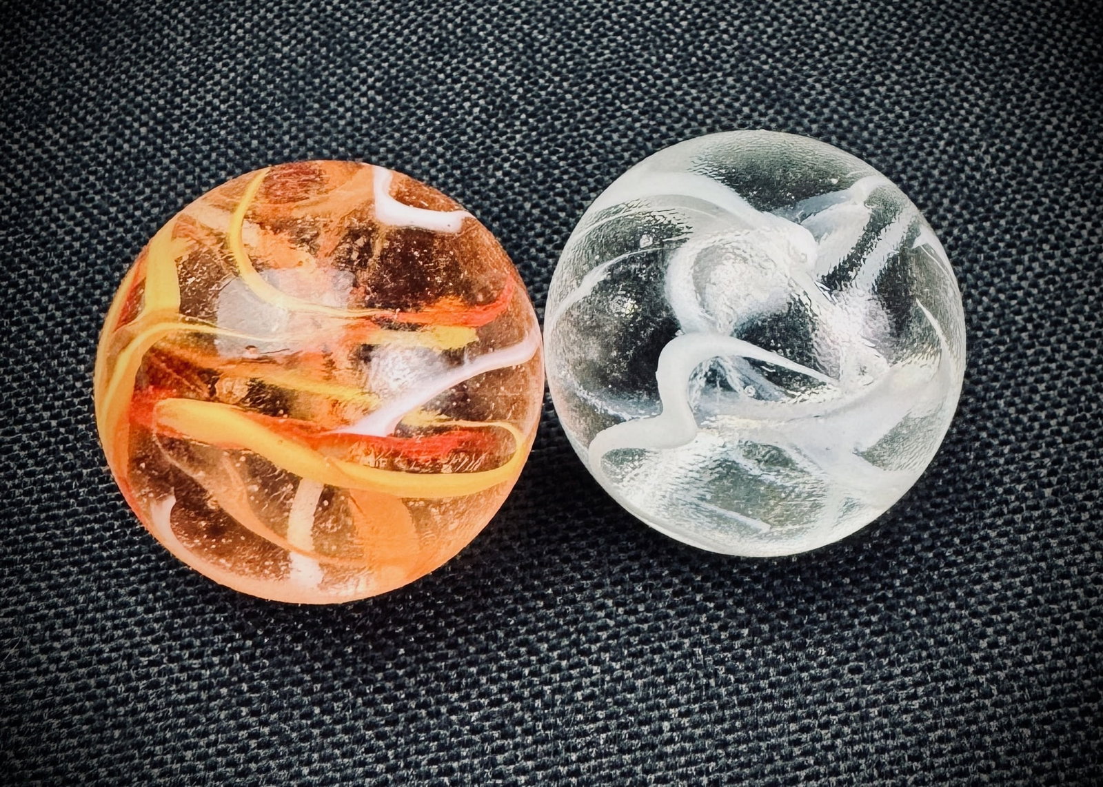 Lot of 2 Swirl Glass Marbles: This lot contains two glass marbles. One is a transparent orange base with white and yellow internal swirls. The other is a clear glass with white internal swirls. Swirl Glass Marble Orange White Yell