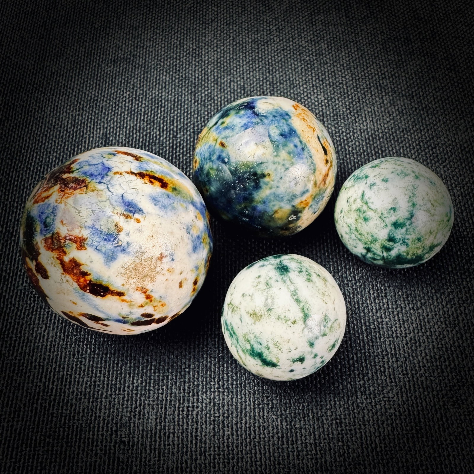 4 Antique Bennington Style Stoneware Marbles: A lot of four antique stoneware marbles in two distinct patterns. Two marbles feature a blue, white, and brown glaze, and two feature a green and white glaze. The largest marble measures approximately