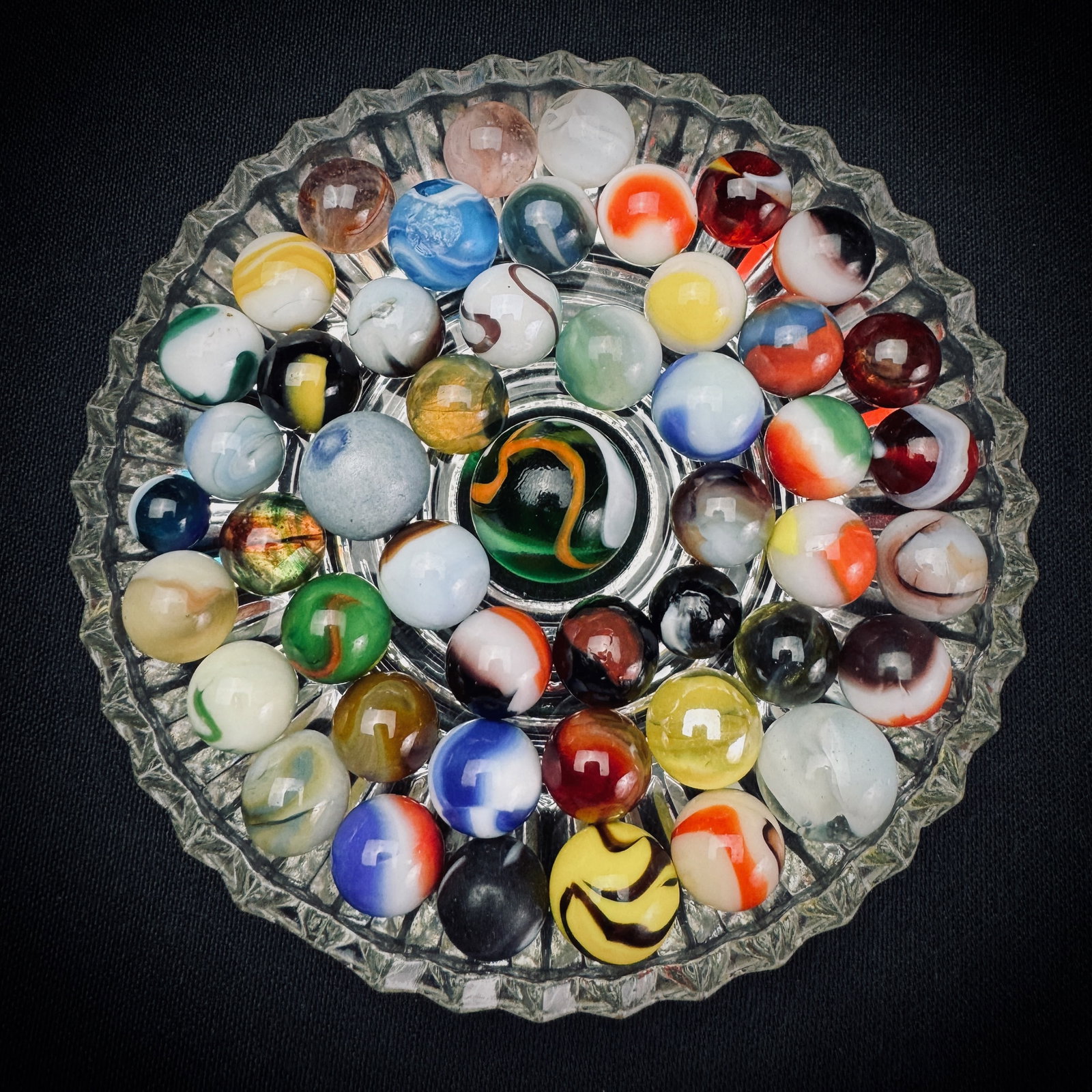 Lot of Assorted Vintage Glass Marbles: This is a lot of assorted vintage glass marbles. The collection features a variety of styles, colors, and patterns including swirls and patches. One larger shooter marble is included with numerous sma