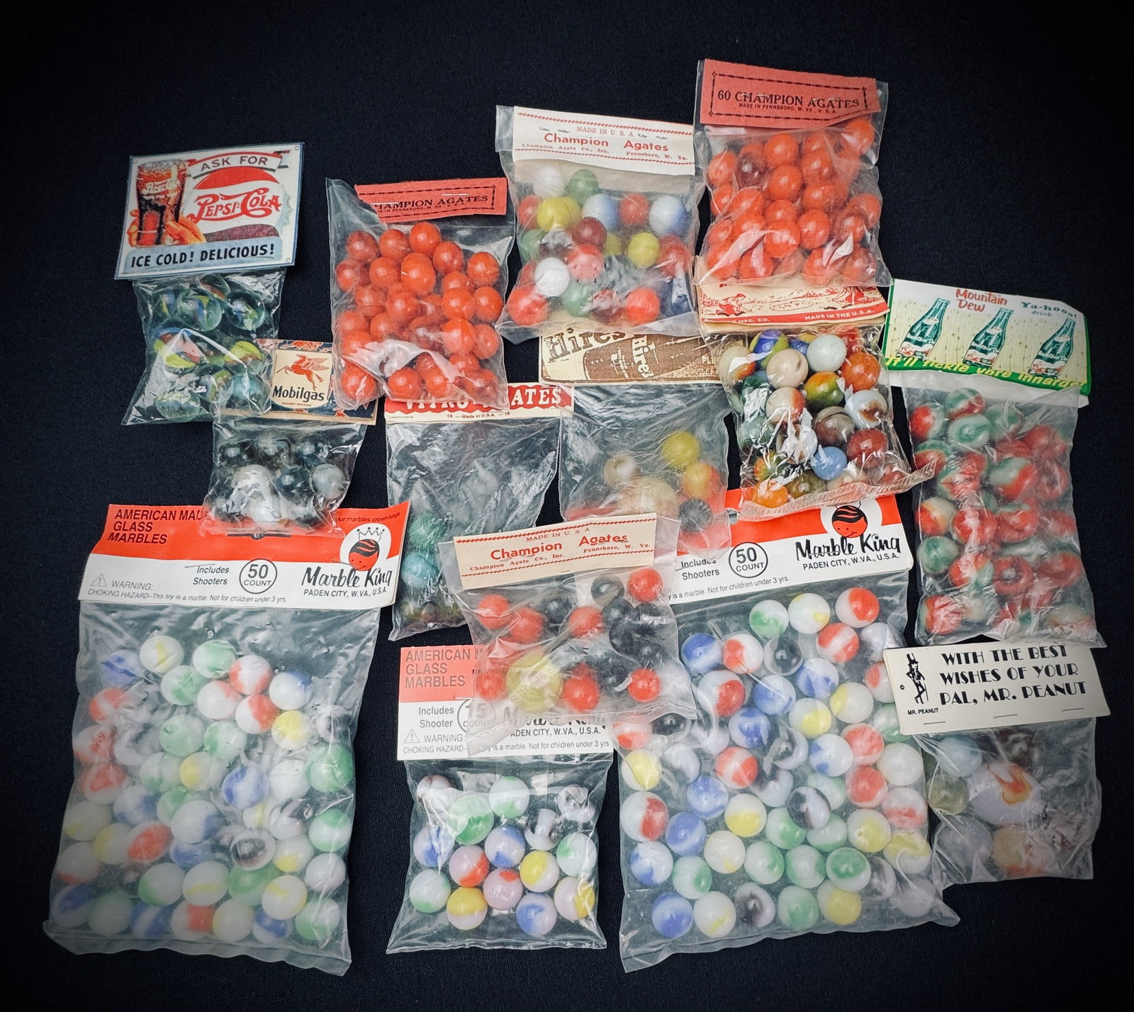 Vintage Glass Marbles in Packaging: This lot contains a collection of glass marbles in their original sealed packaging. Featured brands include Marble King, Champion Agates, Pepsi-Cola, Mobilgas, and Mr. Peanut. The assortment includes