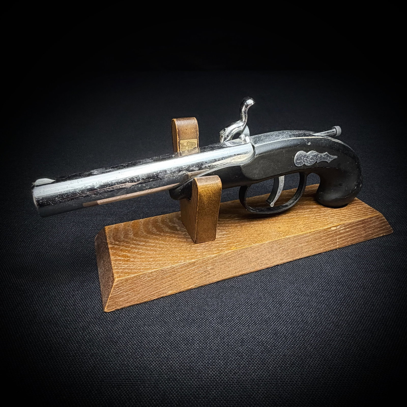 Vintage Flintlock Pistol Table Lighter: This is a vintage table lighter designed in the form of a flintlock style pistol. The piece features a chrome-finished barrel and lock mechanism with a black molded grip. It is presented on a simple w