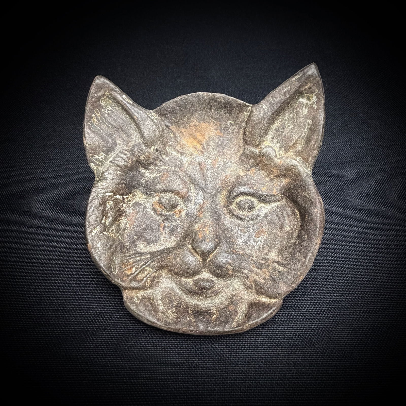 Vintage Cast Metal Cat Head Ashtray: This is a small dish or ashtray made from cast metal in the shape of a cat's head. The front features a detailed, expressive feline face. The shallow bowl could be used as a trinket dish, coin holder,