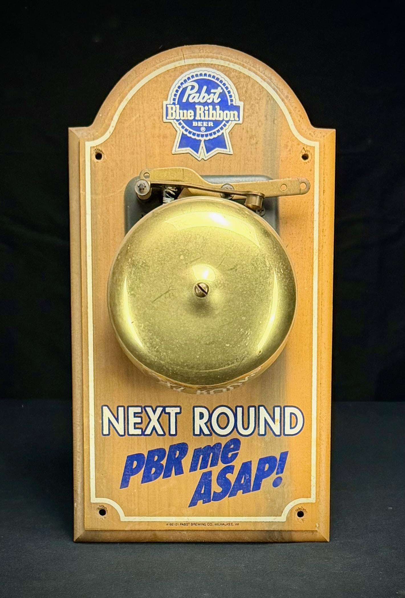 Pabst Blue Ribbon PBR 'Next Round' Bar Bell: This is a Pabst Blue Ribbon promotional bar bell. It features a brass bell and ringer mechanism mounted on a finished wood plaque with the PBR logo. The plaque is screen printed with the phrase 'NEXT