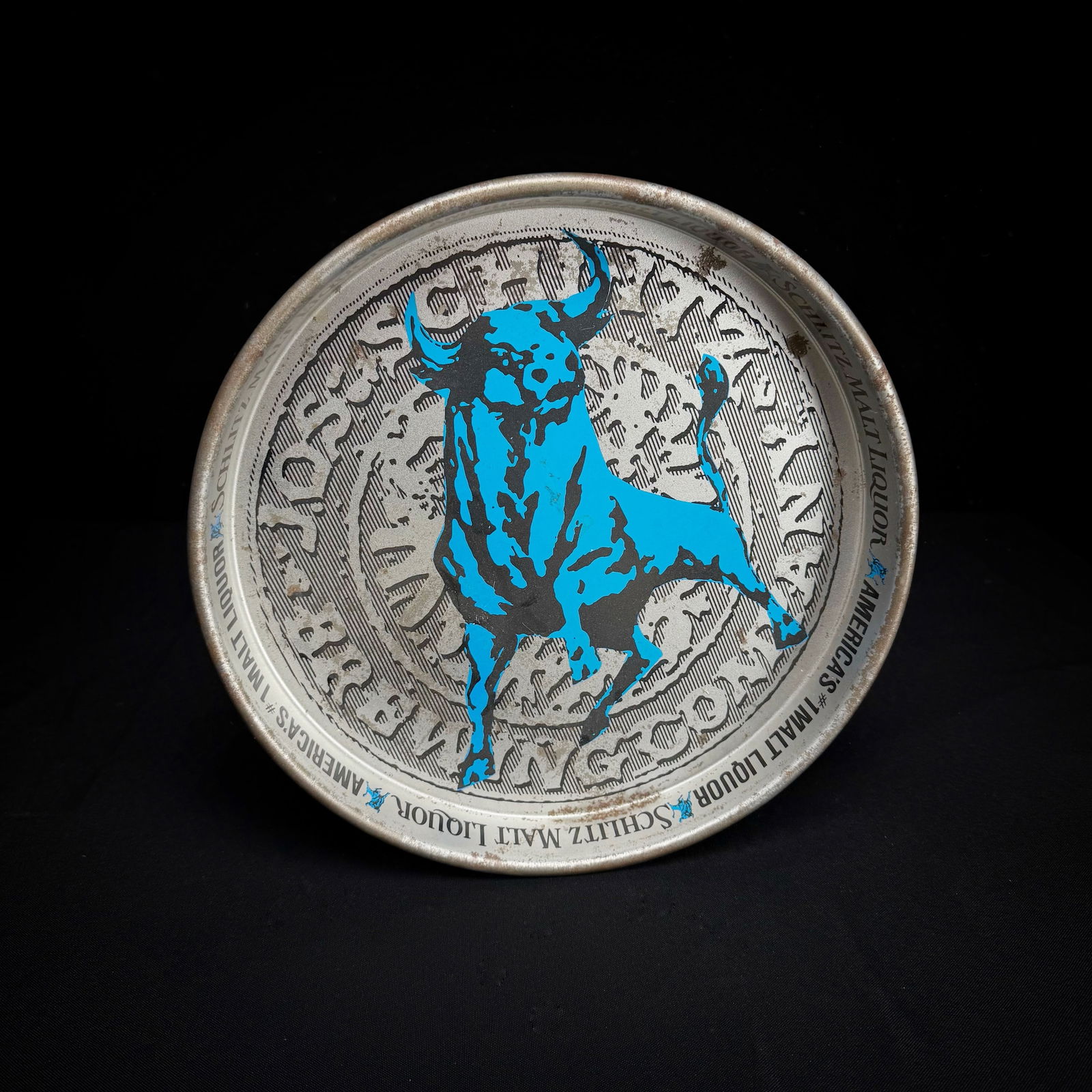 Vintage Schlitz Malt Liquor Bull Tray: This is a metal tip tray or coaster for Schlitz Malt Liquor. It features the brand's bright blue bull logo against a textured background. The rim is printed with 'Schlitz Malt Liquor' and 'America's #