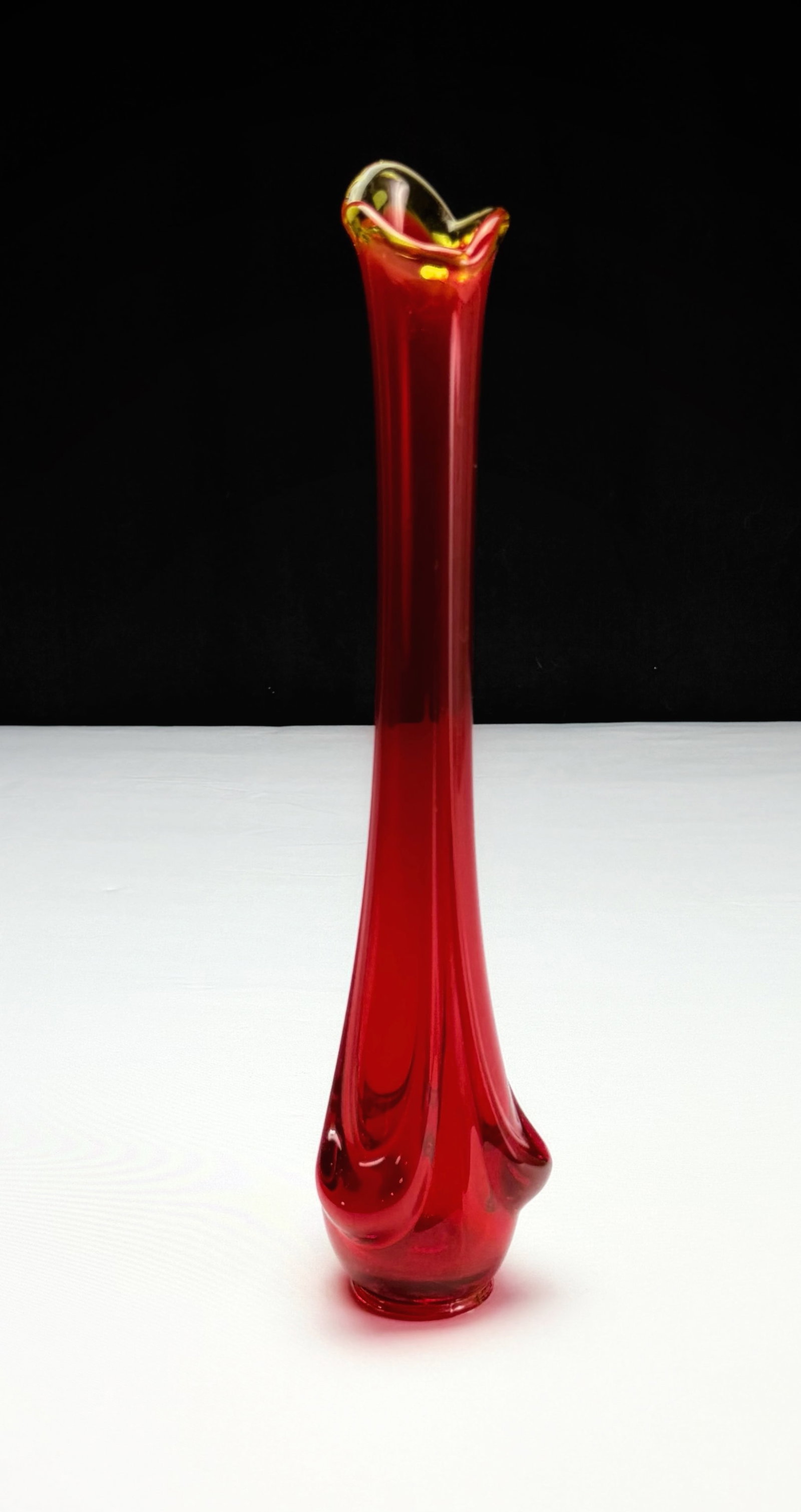 Mid-Century Modern Ruby Amberina Swung Vase: This lot features a mid-century modern art glass vase. The piece exhibits a rich ruby red coloration, transitioning to amberina tones typical of the style. Its elongated form is characteristic of a sw