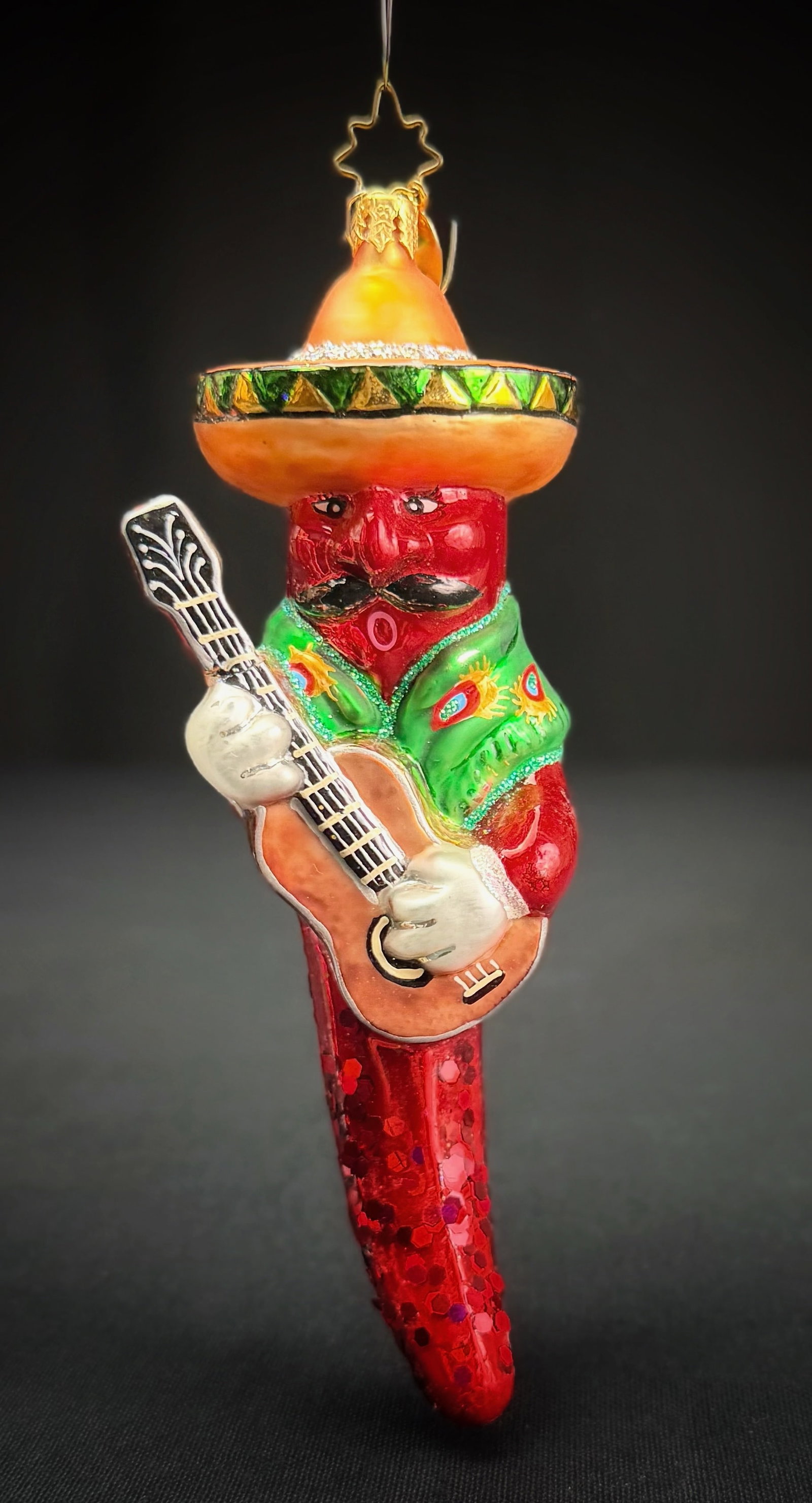Christopher Radko Chili Pepper Ornament: A Christopher Radko handblown glass Christmas ornament titled "Tex Mex Chili Pepper playing guitar." This piece features a red chili pepper figure adorned with a sombrero, a green bandana, and playing