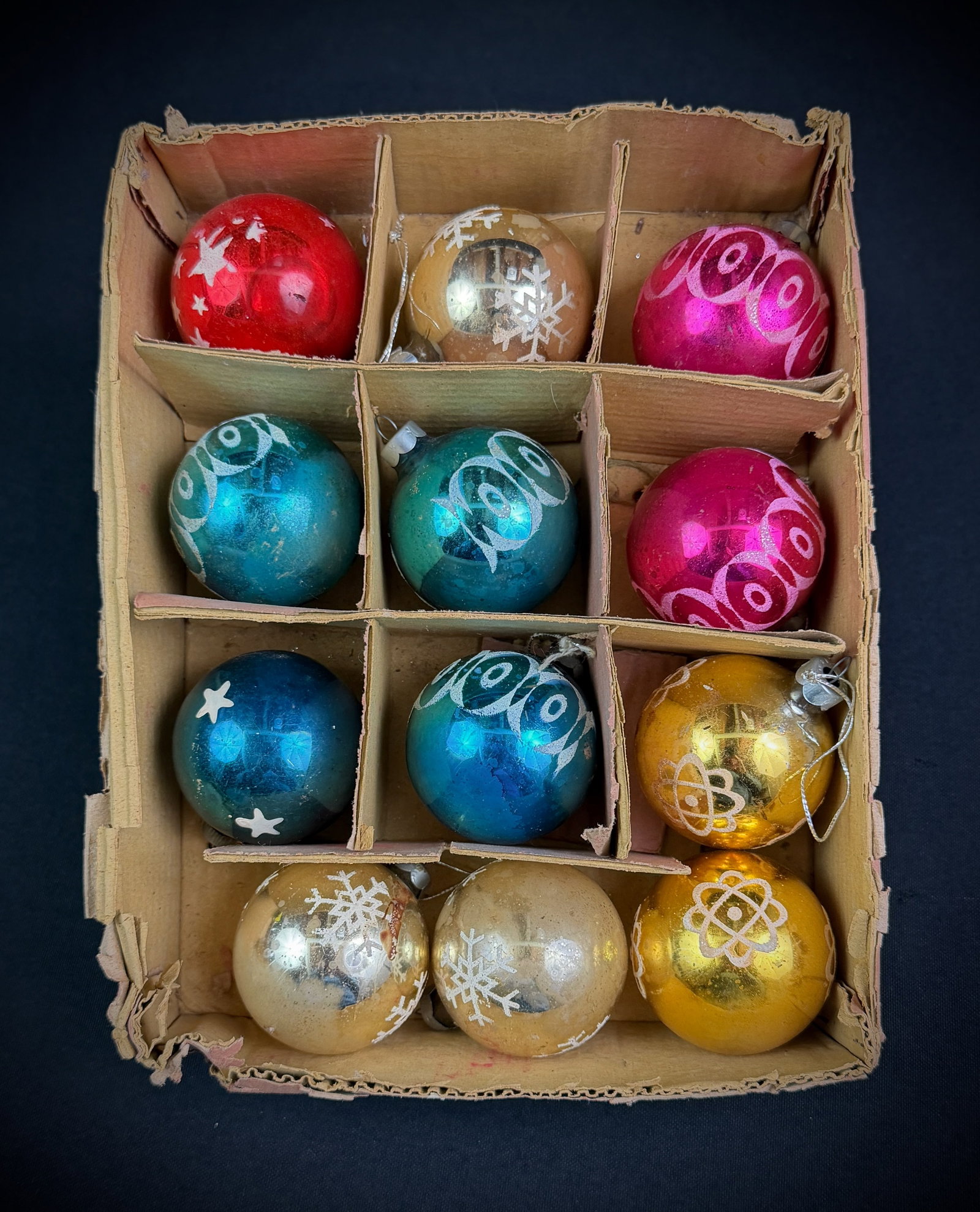 Set of 12 Vintage Glass Christmas Ornaments: A collection of twelve mid-century glass Christmas ornaments housed in the original divided cardboard box. The spherical ornaments are presented in assorted colors including red, blue, pink, gold, and