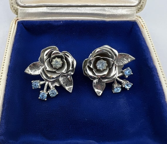 Pair Vintage Coro Rose Motif & Rhinestone Earrings: Pair Vintage Coro Rose Motif & Rhinestone Earrings. Vintage American costume jewelry pair of clip on earrings, rhodium plated, rose flower motif, set with clear and blue rhinestones. Signed on the bac