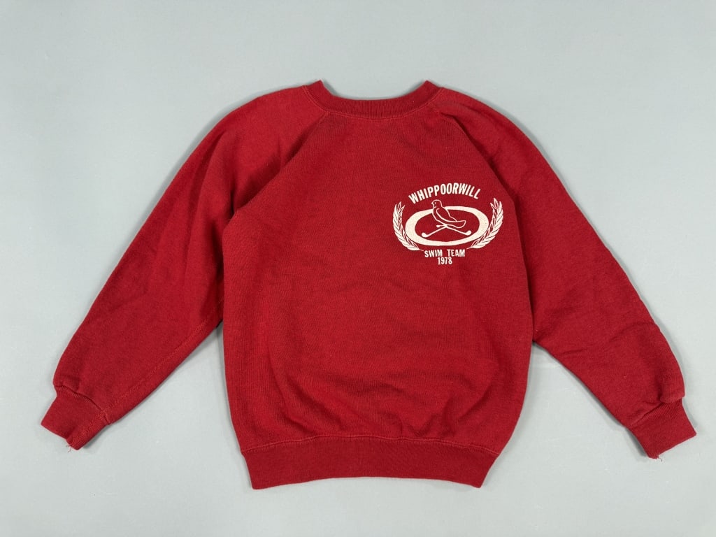 Vintage 1970s Whippoorwill Swim Team Sweatshirt: Vintage 1970s Whippoorwill Swim Team Sweatshirt having graphic at chest, crew neck, and raglan sleeves. Champion blue bar tag marked M 10-12. Measuring 16 inches flat across chest, 20 inches long, 20