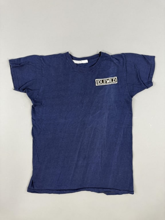 Vintage 1970s Idlewild Blue Tee Shirt: Vintage 1970s Idlewild Blue Tee Shirt having IDLEWILD patch sewn on chest. Measuring 17 inches flat across chest, 22 inches long, 5 inch sleeve length with stretch throughout.