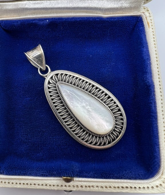 Sterling Silver Filigree Pendant w Mother of Pearl: Sterling Silver Filigree Pendant with Mother of Pearl.Having two filigree borders with coiled wire wrap design between and bezel set at center with a teardrop mother of pearl cabochon. Hallmarked on t