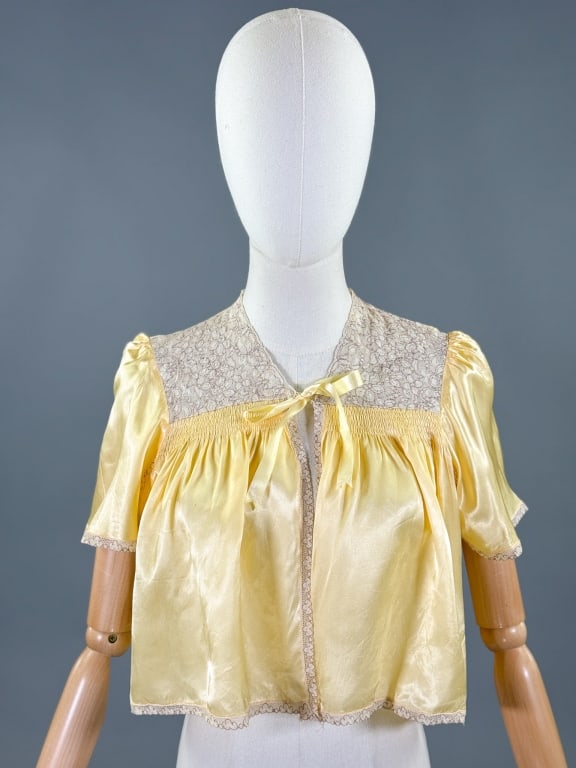 Vintage 1930s Yellow Rayon Satin Lace Bed Jacket: Vintage 1930s Yellow Rayon Satin Lace Bed Jacket having lace details throughout with ruched bust, short puffed sleeves, and single ribbon tie at front. Measuring free bust, 16 inches long, 9 inch slee