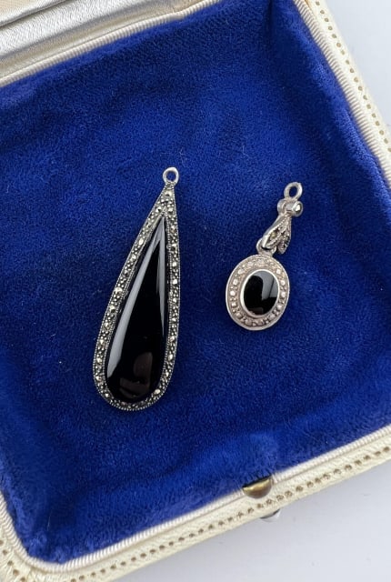 Art Deco Style Sterling Onyx Marcasite Pendants: Art Deco Style Sterling Onyx Marcasite Pendants or Charms. One tear drop necklace pendant and one oval with ornate and articulated bail. Larger is hallmarked and measures 1.75 inches in length.