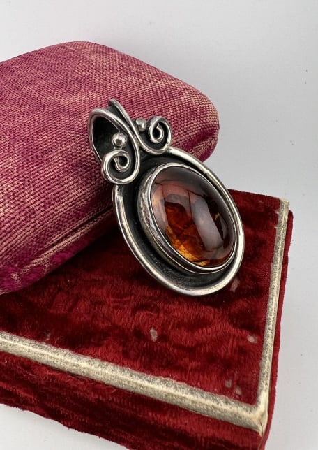 Arts & Crafts Style Sterling Amber Pendant: Arts & Crafts Style Sterling Silver Amber Necklace Pendant. Hallmarked 925 on the back. Set with a large cabochon amber. Measures 2 inches in length.
