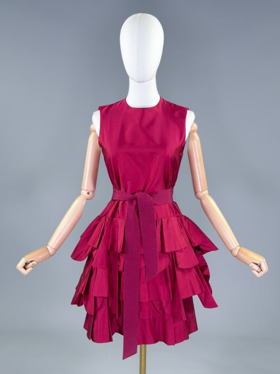 Vintage Moschino Drop Waist Tiered Ruffle Dress: Vintage Moschino Drop Waist Tiered Ruffle Dress having sleeveless armholes, round neckline with single button closure at back, tiered ruffled skirt and grosgrain ribbon belt at waist. Labeled Moschino