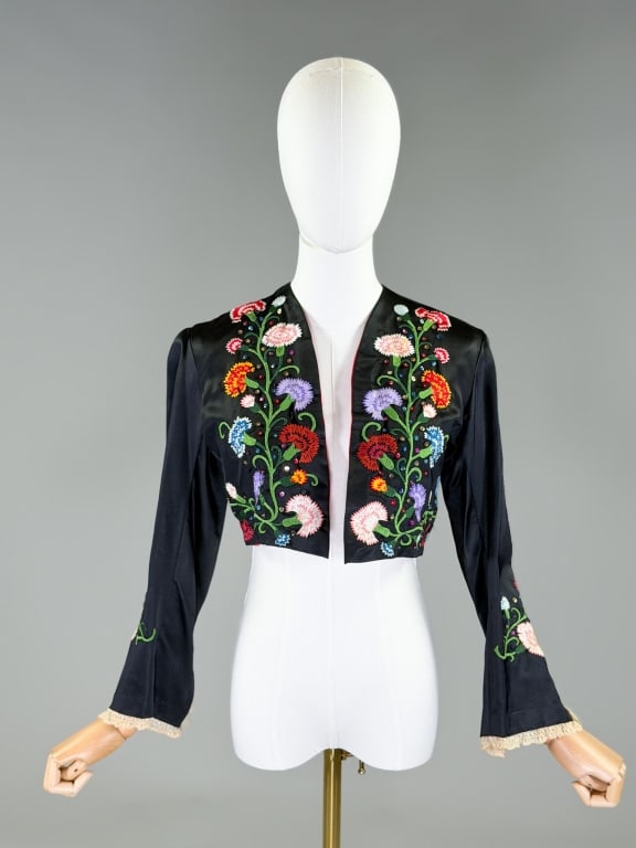 Vintage Floral Embroidered Satin Bolero Jacket: Vintage Floral Embroidered Satin Bolero Jacket having open front with floral embroidery, lace details at sleeve cuffs, and fully lined throughout. Measuring 15 inches long, 21 inch sleeve length. From