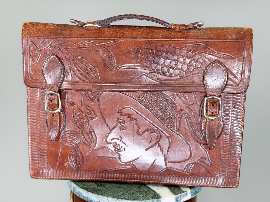 Vintage 1970s Mexican Tooled Leather Briefcase Bag: Vintage 1970s Mexican Tooled Leather Briefcase Bag having tooled detail at front with buckle closure and top handle. Measuring approximately 11 inches high by 15 inches wide by 3 inches deep. From the