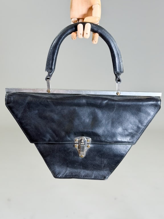 Vintage 1980s Leather Trapezoid Handbag: Vintage 1980s Leather Trapezoid Handbag having metal toggle closure at front with metal frame at top. Measuring approximately 10 inches high by 16 inches wide by 2 inches deep. From the lifetime colle