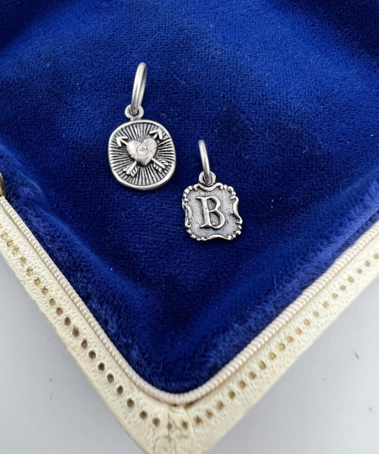 Two Sterling Silver Charm Pendant by Waxing Poetic: Two Sterling Silver Charms or Pendants by Waxing Poetic. Signed WP and hallmarked. B monogram charm and heart with crossed arrows charm. Larger measures approximately 1 inch in length with the bail.