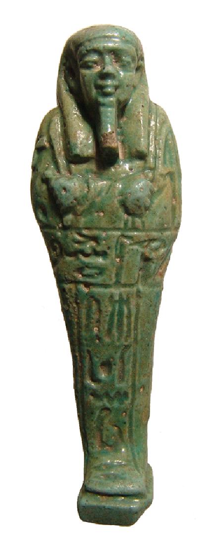 An Egyptian green faience ushabti, Late Period: An Egyptian green faience ushabti, Late Period, c. 664 - 332 BC, mummiform with integral base, wearing tripartite wig and false beard, arms folded at chest, hands holding a pick and hoe, bag over left