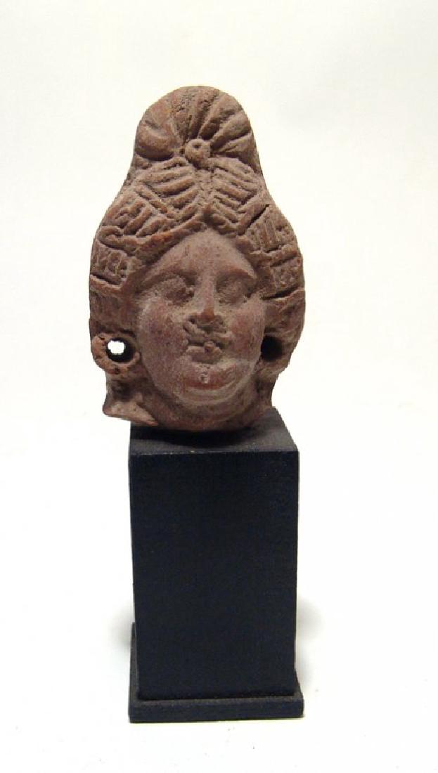 An Egyptian terracotta head of a woman, Ptolemaic: An Egyptian terracotta head of a woman, Ptolemaic, c. 3rd - 1st Century BC, her hair nicely styled into a coiled plait at the back of the head, her features attractive and ears with holes for earrings