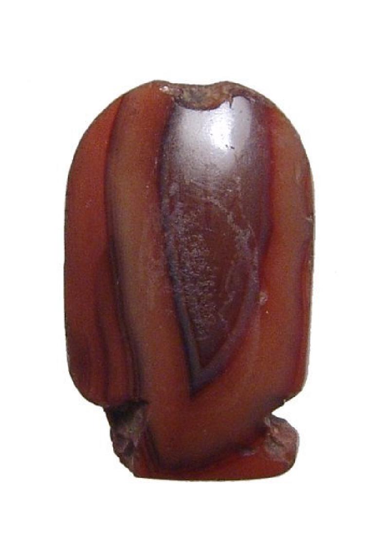 An Egyptian carnelian cartouche-shaped bead: An Egyptian carnelian cartouche-shaped bead, c. 1570 - 30 BC, in lovely banded stone with good color, the sides well-polished with hole drilled lengthwise for suspension. H: 1 1/5 in (3cm). Ex Boston 
