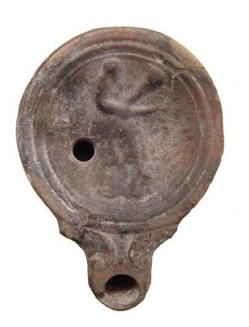 An interesting Roman lamp with seated male figure: An interesting Roman lamp with seated male figure, 1st Century AD, holding an uncertain object, perhaps a tool or weapon. The volute nozzle with rounded tip, the inward sloping shoulder separated from