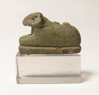 A well-detailed Egyptian green faience amulet of Khnum: A well-detailed Egyptian green faience amulet of Khnum, Late Period, c. 664 - 30 BC, in reclining position, his head well-modeled, remnants of suspension loop on back. L: 25 mm. On lucite base. Ex