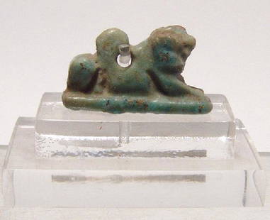 Egyptian green-glazed amulet of recumbent lion: An Egyptian light green-glazed faience amulet of recumbent lion, Late Period, c. 664 - 30 BC, with good detail and suspension loop on back. L: 2.2 cm. With custom lucite base with collection label.