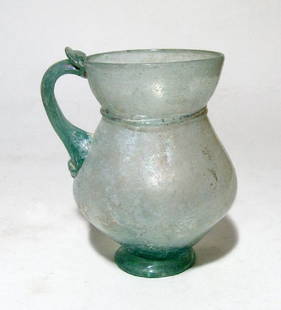 Beautifully formed Roman pale green glass handled cup: A beautifully formed Roman pale green glass handled cup, c. 4th Century AD, the pear-shaped body with flared foot, narrow neck with horizontal ridge and flared mouth, a single handle in the same color