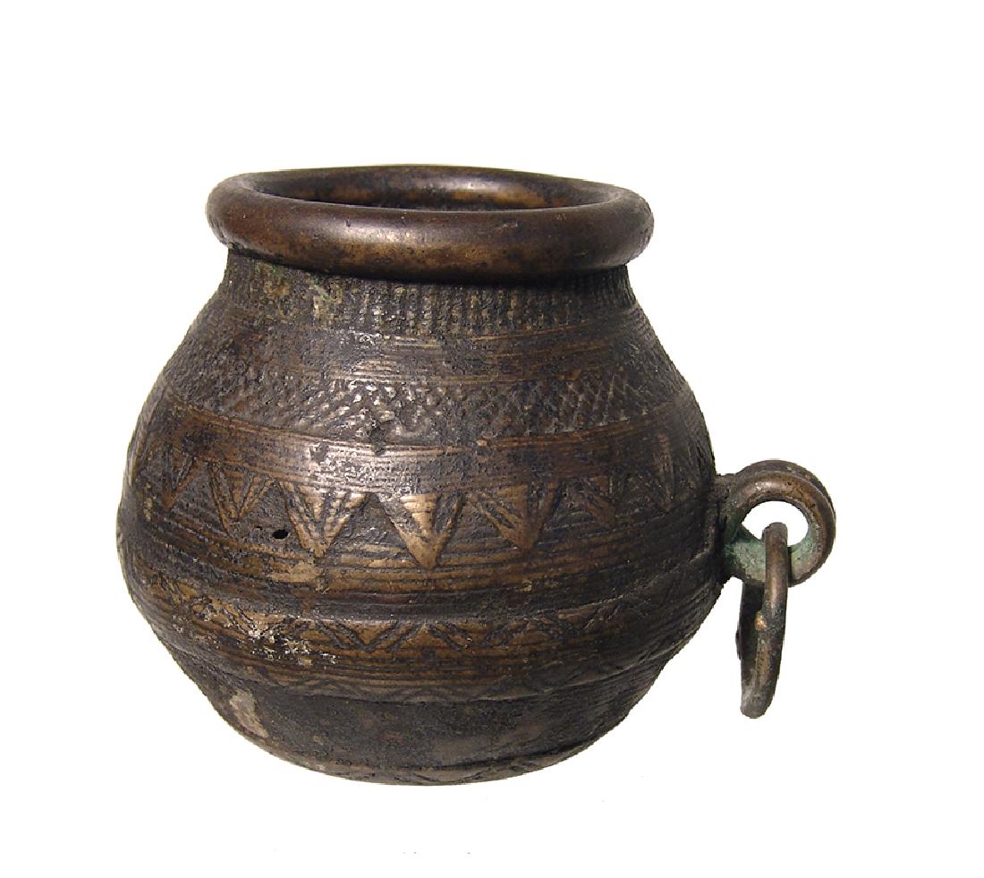 An antique brass/bronze jar, Near East: An antique brass/bronze jar, Near East, c. 18th - 19th Century, with raised geometric decoration, a rounded rim and a small loop handle with a suspended ring; the bottom notable with a beautiful radia