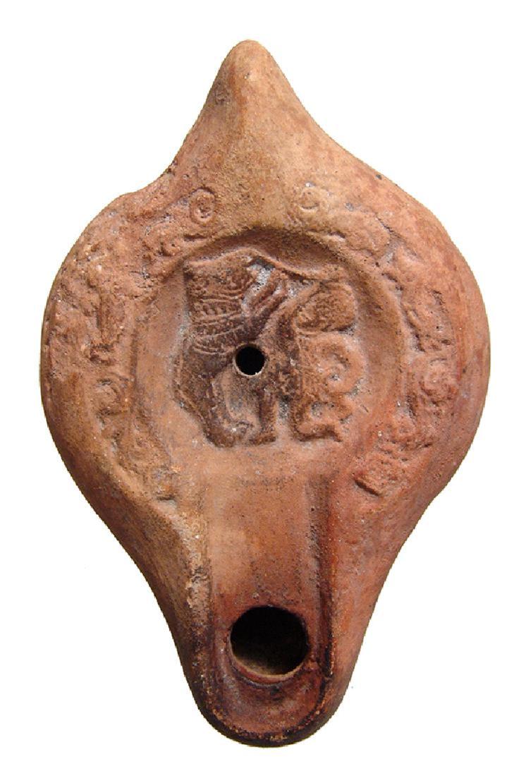 Roman terracotta discus lamp with gladiator and bear: A Roman terracotta discus lamp depicting a gladiator fighting a rampant bear, North Africa, 5th - 6th Century AD, the central scene within the discus, the shoulders adorned with floral devices. L: 4 1