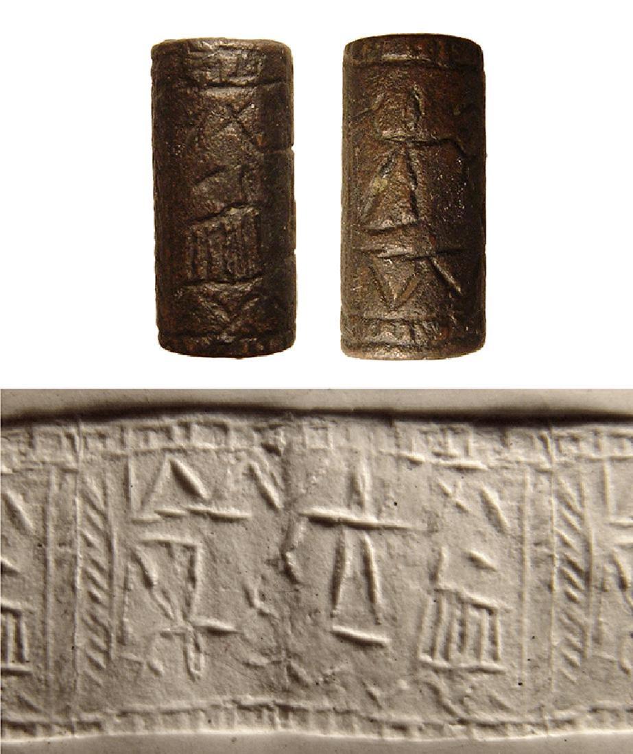 A Levantine hematite cylinder seal: A Levantine hematite cylinder seal, c. 2nd Millennium BC, with a schematized scene depicting standing figures, one inverted and a horned goat, uncertain objects around; all within a hatched and herrin