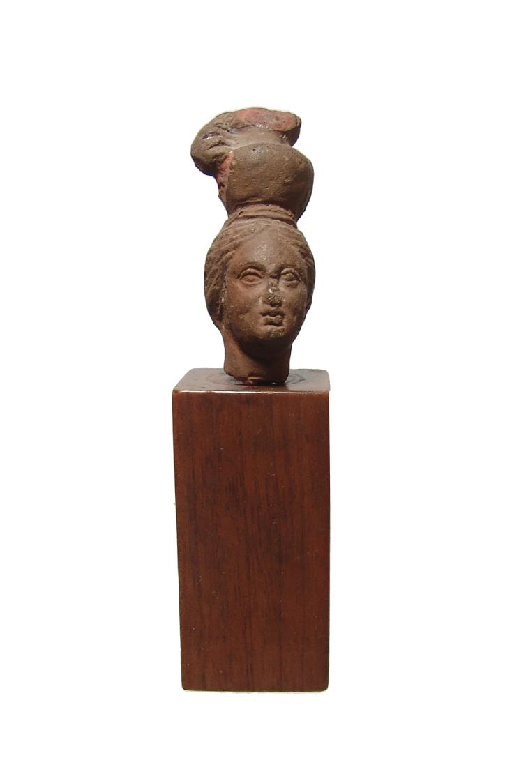 Egyptian terracotta head of a woman with ewer: An Egyptian terracotta head of a woman with an ewer on head, Ptolemaic, c. 2nd - 1st Century BC, her features in fine style, her hair styled back to a coiled plait at the back of her head. H: 2 2/5 in
