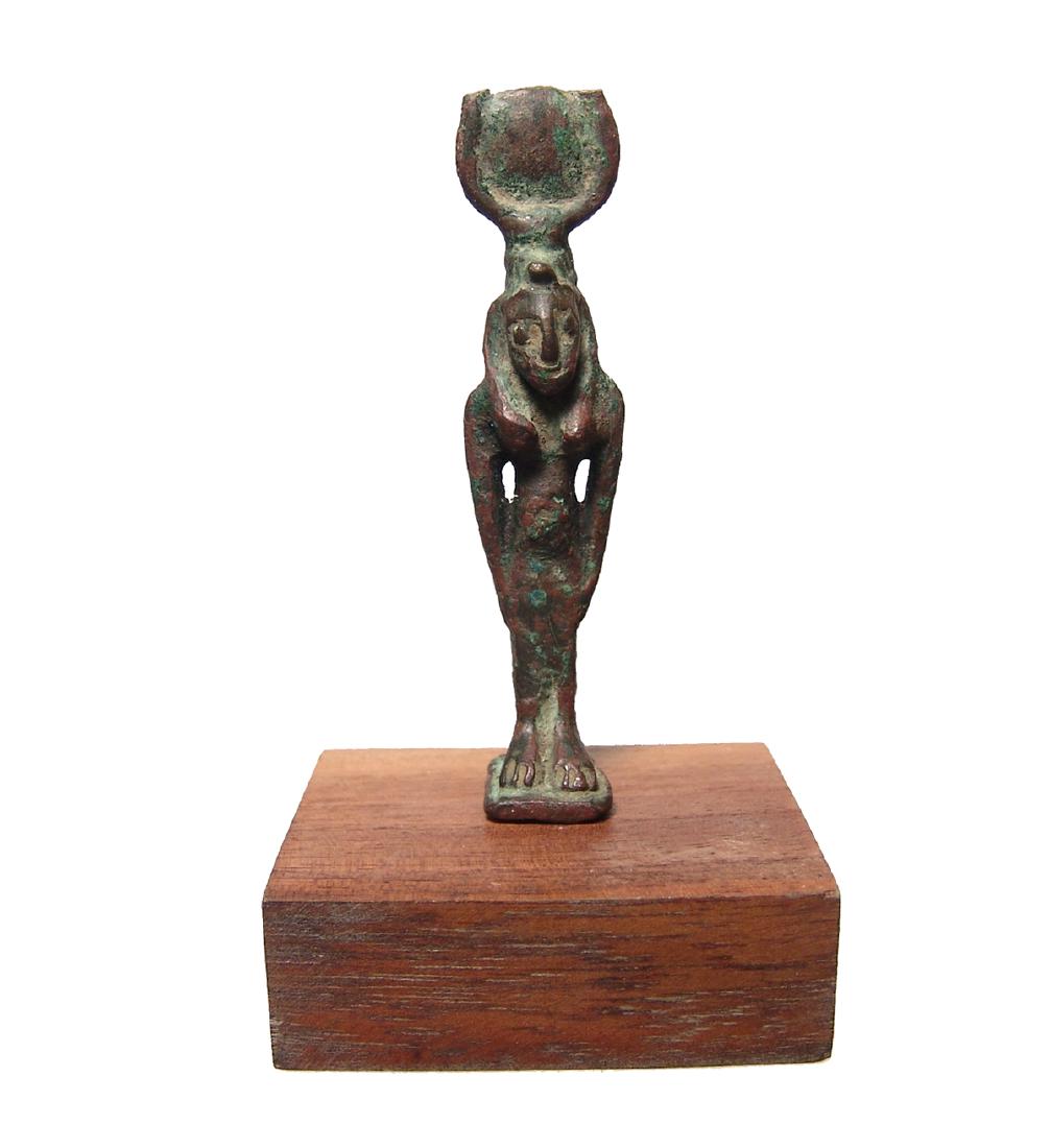 An Egyptian bronze figurine of Hathor, Late Period: An Egyptian bronze figurine of Hathor, Late Period, c. 664 - 332 BC, standing on integral base, wearing tight-fitting gown and wig with uraeus and a headdress consisting of a solar disk between cow's 