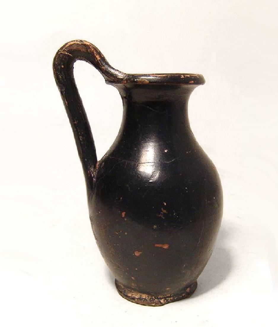 A Greek black glazed olpe: A Greek black glazed olpe, 4th - 3rd Century BC, of graceful form with high handle and nice glossy black surfaces. H: 4 1/4 in (10.8 cm). Ex Christopher Terry collection.