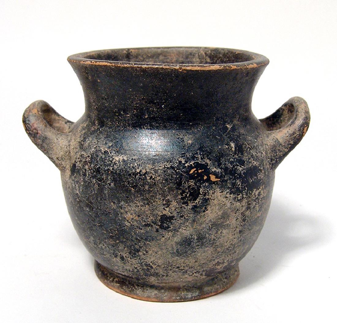 A Greek black-glazed stamnos: A Greek black-glazed stamnos, 4th Century BC, the body rounded with flared ringed foot, short neck with flared mouth and two horizontal handles. H: 3 7/8 in (9.9cm). Moderate surface deposits. Ex coll