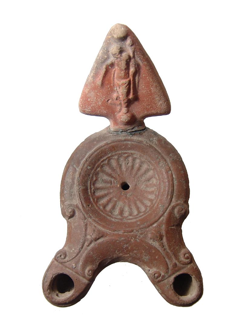 A Roman double spouted ceramic lamp: A Roman double spouted ceramic lamp, 2nd Century AD, with a central rosette within the discus, the spout long and rounded and adorned with volutes. The handle, which is originally from a separate lamp