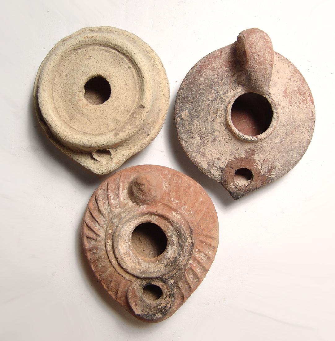 A group of 3 ceramic lamps from the Holy Land: A group of 3 ceramic lamps from the Holy Land. Lot includes a Byzantine type, c. 6th - 7th Century AD, with raised lines around the shoulders, conical handle and beautiful decorated cruciform device a