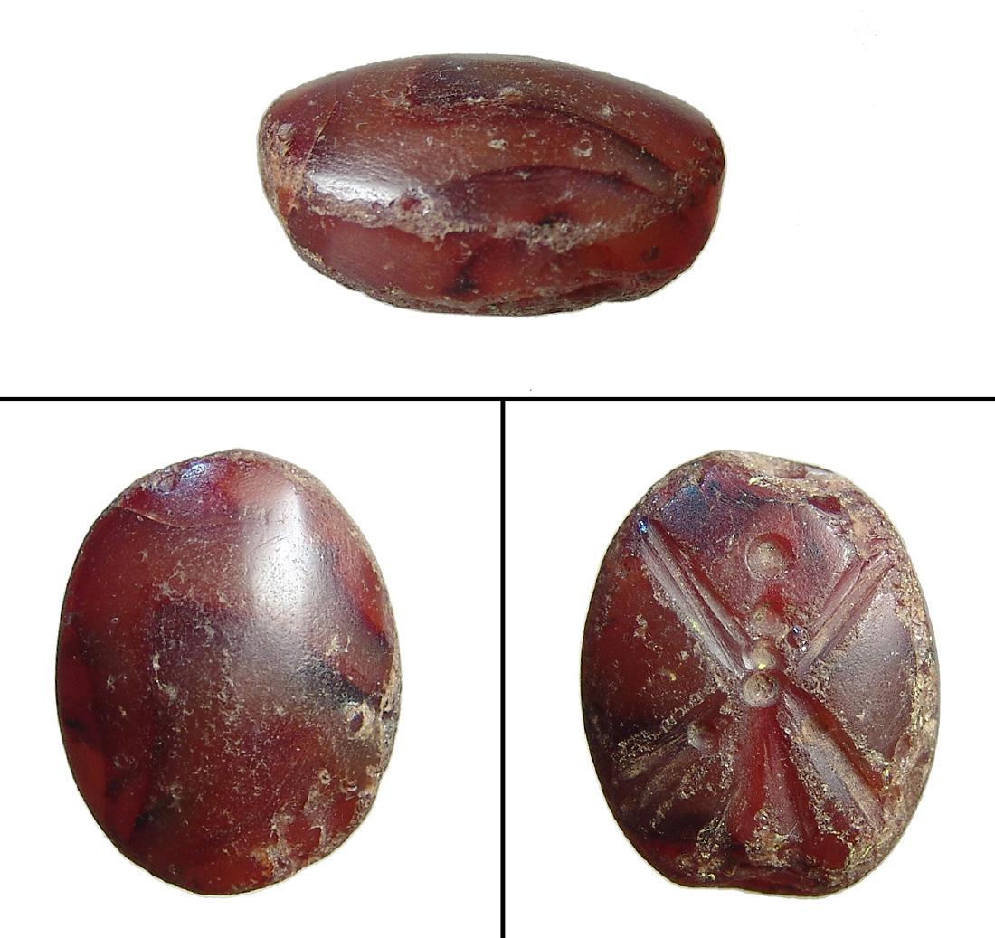 A Neo-Assyrian carnelian scaraboid: A Neo-Assyrian carnelian scaraboid, c. 9th - 7th Century BC, carved from deeply colored stone with suspension hole drilled lengthwise, on base a standing winged deity, possibly Pazuzu. 22 x 18 mm. Ex 