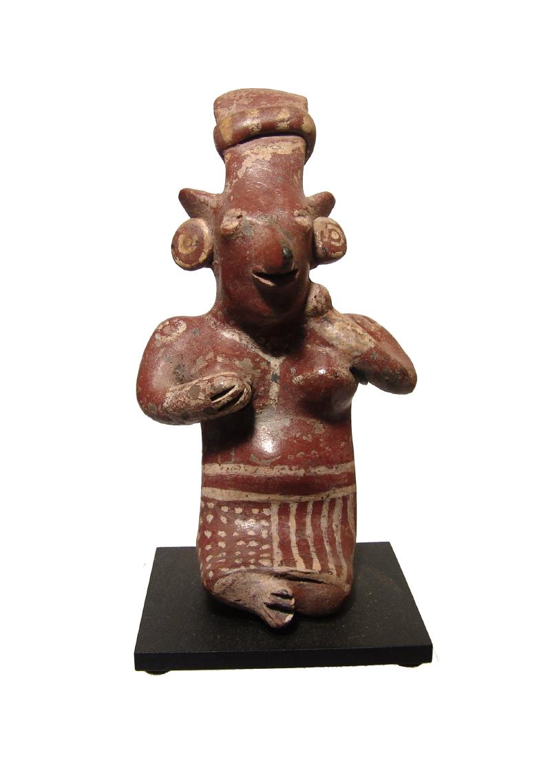 A charming Jalisco sheep face sitting woman: A charming Jalisco sheep face’ sitting woman, West Mexico, c. 100 BC - AD 200, placing her right hand on her breast and left hand on her neck, wearing a headband and skirt; her ears adorned with lar