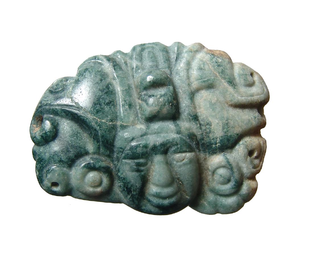 A lovely Mayan jade pendant in the form of a head: A lovely Mayan jade pendant, c. AD 600 - 800, carved in the form of a facing head wearing an elaborate headdress and earspools. The piece beautifully incorporates the shape of the stone and is drilled