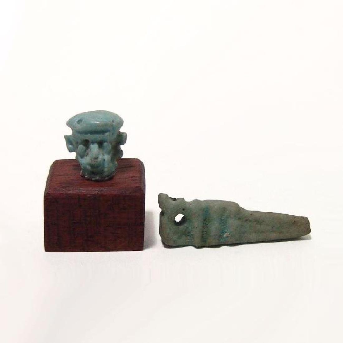 Egyptian faience Pataikos head and crocodile amulet: An Egyptian faience head of Pataikos and a crocodile amulet, Ptolemaic, c. 332 - 30 BC, the head with detailed features and remnants of light blue glaze. 14 x 11 mm. With little wood base. The crocodi