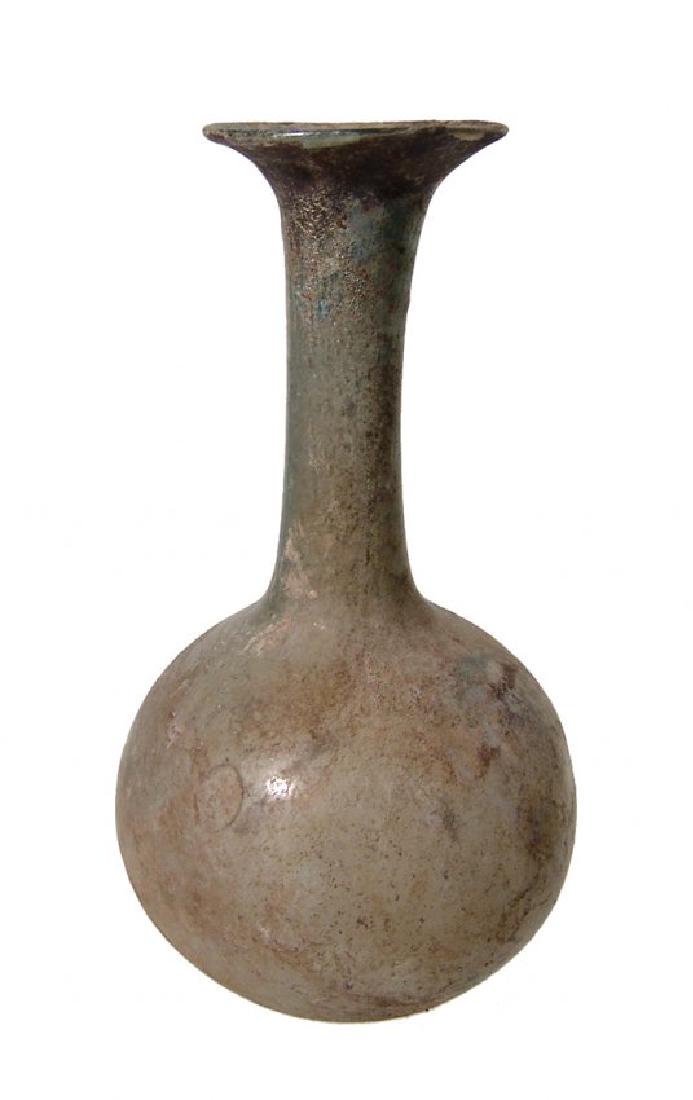 A nice Roman pale-yellow glass bottle: A nice Roman pale-yellow glass bottle, 1st - 2nd Century AD, the body round with indented base, long cylindrical neck surmounted by a widely flared mouth and rounded rim. H: 4 3/8 in (11.2 cm). Well p