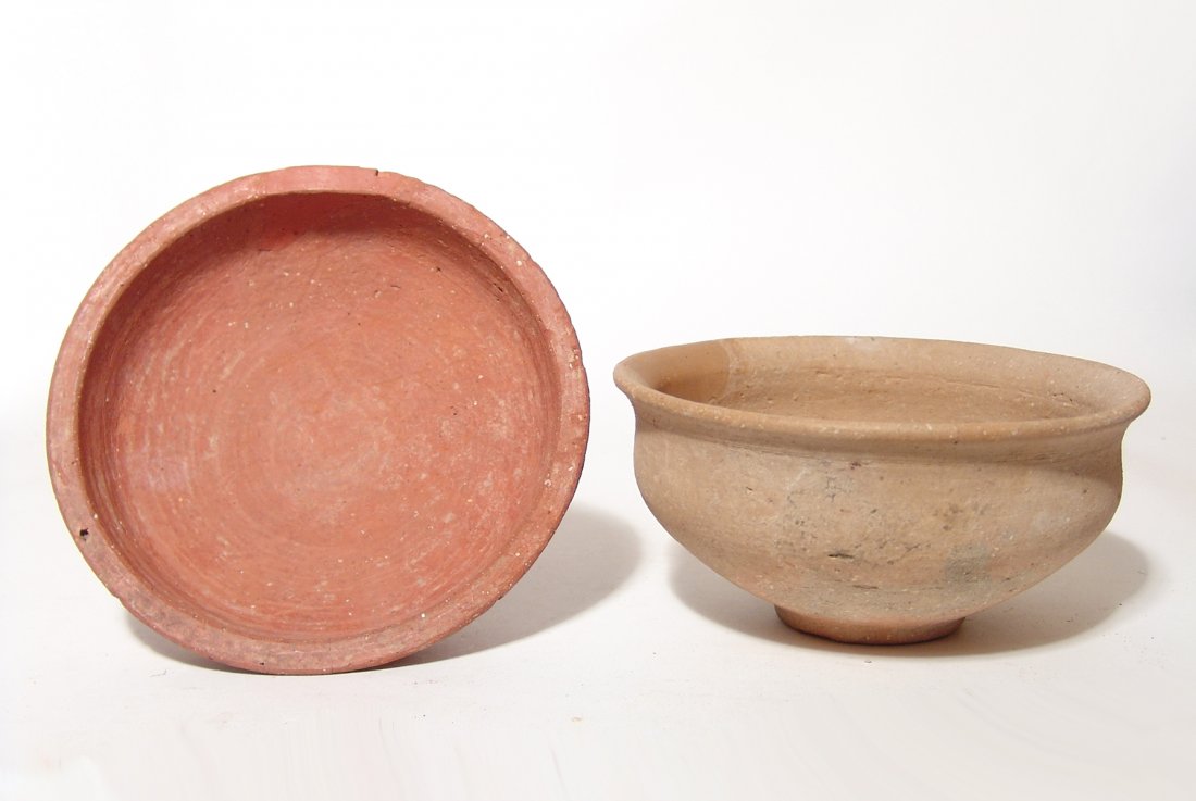 A pair of Late Bronze Age bowls: A pair of Late Bronze Age bowls, c. 1550 - 1200 BC, the first of lower profile in a deep orange ware, 2 x 6 1/2 in (5 x 16.4 cm), the second a creme buff bowl with narrow pad base and flared rim, 3 1/