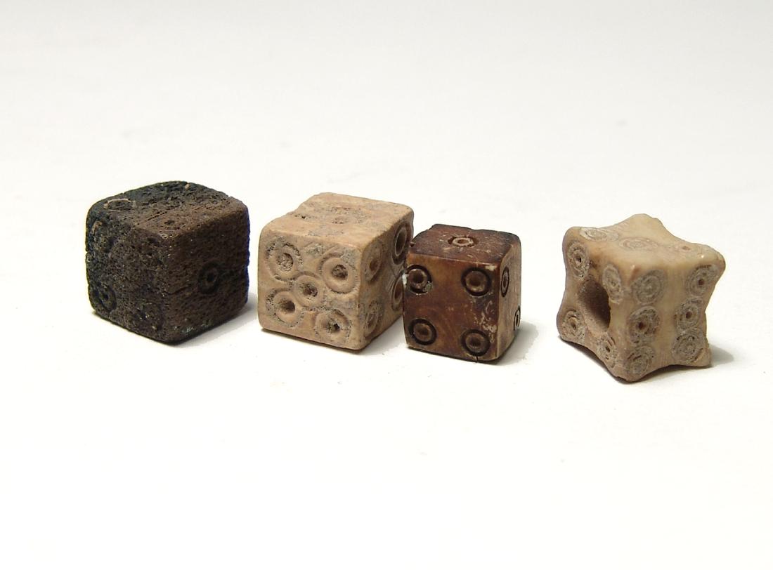 A group of 4 Roman bone dice: A group of 4 Roman bone dice, c. 1st - 3rd Century AD, of classic form with drilled circles around a central divot aligned 1 - 6 on the six sides. One with concave edges and a central hole where it pe
