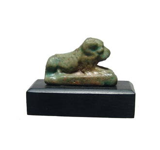 Egyptian faience glazed amulet of a recumbent lion: An Egyptian faience glazed amulet of a recumbent lion, Late Period, c. 664 - 30 BC, on integral rectangular base with nice detail and good green color. 23 x 15 mm. Mounted on old wood base. Ex